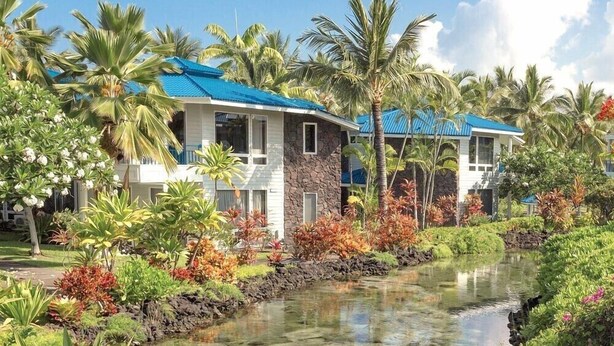 Ein Resort mit mehreren Gebäuden, einem kleinen Wasserspiel und tropischer Bepflanzung.