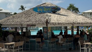 A beachside bar with a thatched roof, overlooking a pool.