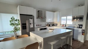 A modern kitchen with white cabinetry, a central island with bar stools, a built-in oven, and a microwave above the island.