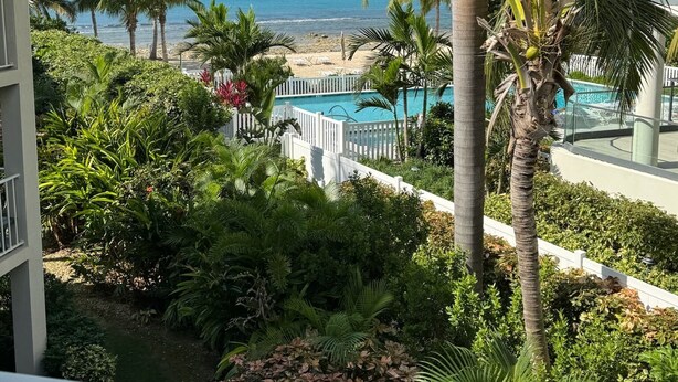 A view of a beach resort with a pool, palm trees, and a clear blue sky.