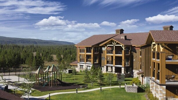 A multi-story building with a central courtyard, surrounded by a park with playground equipment. - WorldMark Yellowstone - 1 Bedroom (West Yellowstone)