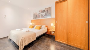 Una habitación de hotel con una cama grande, dos mesitas de noche con lámparas, un armario de madera y una obra de arte con un paisaje urbano en la pared.