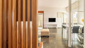 Una sala de estar moderna con un separador de madera, un televisor de pantalla plana, una zona de comedor con una mesa y sillas, y un banco.