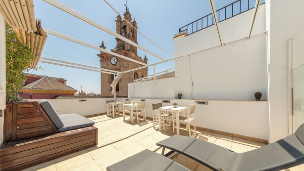 Terraza en la azotea con sillones de descanso, mesas y vistas a una torre de reloj histórica.