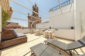Una terrazza sul tetto con poltrone lounge, tavoli e vista su un'antica torre dell'orologio.