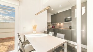 Una cocina moderna con armarios grises, un microondas de acero inoxidable y una mesa de comedor blanca con sillas.