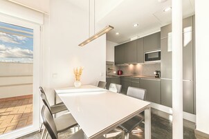 Una cocina moderna con armarios grises, un microondas de acero inoxidable y una mesa de comedor blanca con sillas.