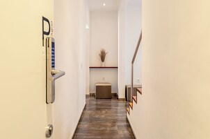 A hallway with a modern door, a small seating area, and a decorative vase on a shelf.