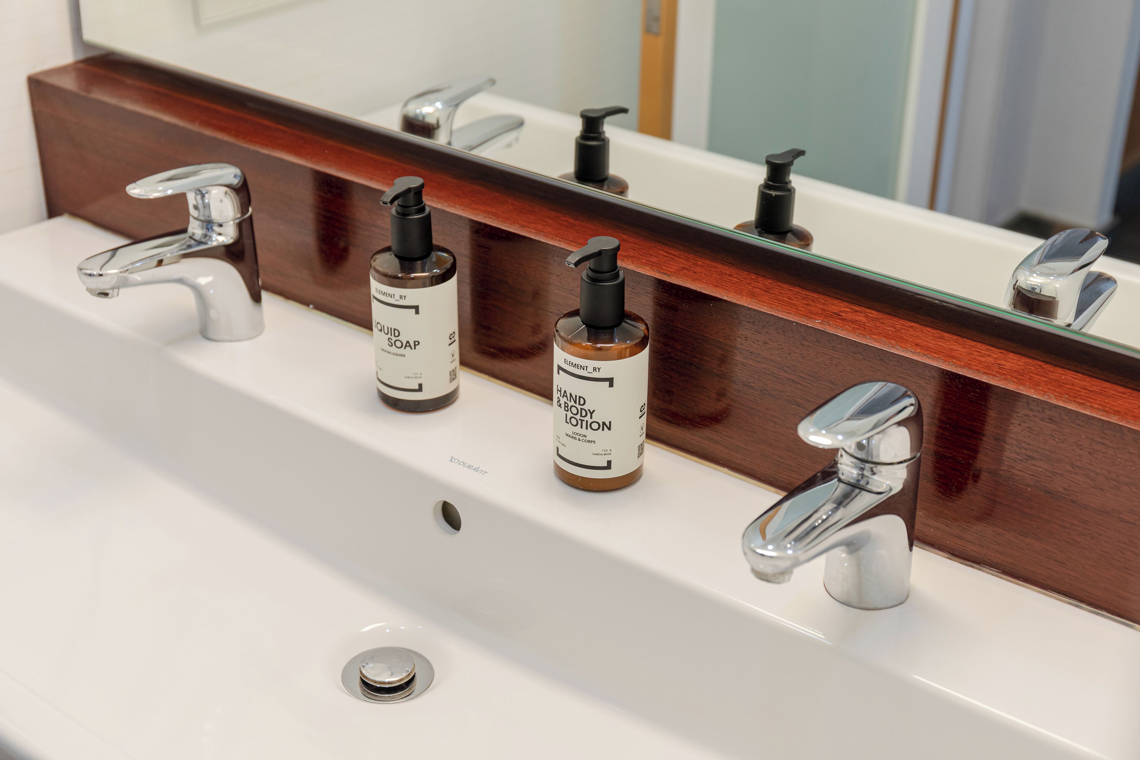 Un lavabo de salle de bain avec deux distributeurs de savon et un miroir au-dessus.