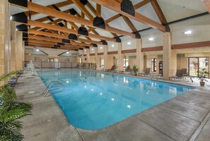 An indoor swimming pool with wooden beams, lounge chairs, and potted plants.