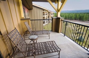 Ein Balkon mit zwei Metallstühlen und einem kleinen Tisch, der auf einen bewaldeten Bereich und ein Gebäude im Hintergrund blickt.