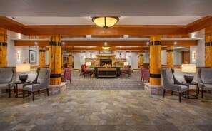 Eine Lobby mit Steinboden, Holzsäulen und einem Kamin im Zentrum.
