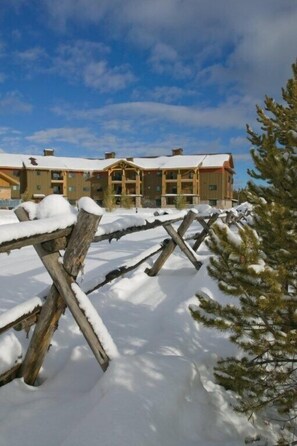 Ein mit Schnee bedeckter Holzzaun vor einer Lodge mit zahlreichen Fenstern und einem schneebedeckten Dach.