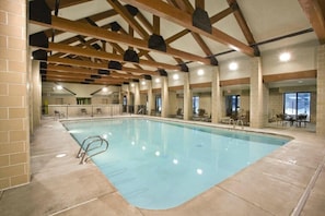 An indoor swimming pool with a tiled floor, wooden beams, and seating areas. - Yellowstone | Adventure Base Stay | Pool + Nature (West Yellowstone)