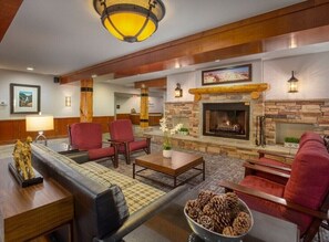 Eine geräumige Lobby mit Kamin aus Stein, roten Polstersesseln und einem Holztisch.