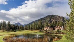 Un chalet avec un étang, entouré d’un parcours de golf et de montagnes.