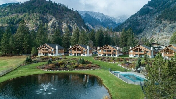 Un chalet doté de plusieurs cabanes en bois, d’un étang et d’une piscine, le tout entouré de montagnes et d’arbres.