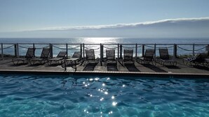 Ein Poolbereich mit Liegestühlen und Blick aufs Meer.