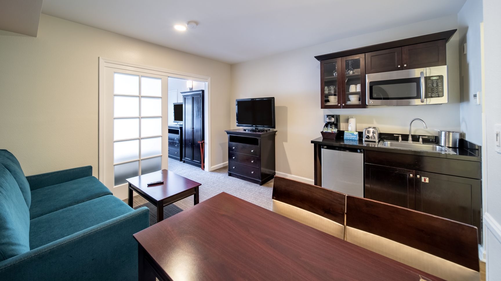 A compact living space with a kitchenette, a television, a sofa, and a dining table.