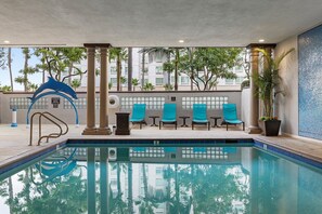 A pool area with a dolphin sculpture, lounge chairs, and a tiled wall.