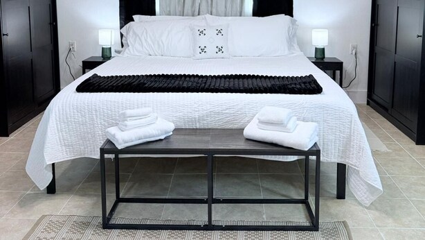 A modern bedroom with a bed, bedside tables, a bench, and a ceiling fan. - Serenity @ Court (Sanford)