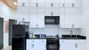 A modern kitchen with white cabinets, a black refrigerator, a microwave, a stove, and a sink. - Serenity @ Court (Sanford)