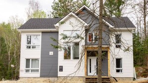 A two-story house with a gabled roof, white siding, and a front door with a small porch.