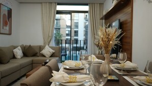 Ein Essbereich mit Tisch für zwei Personen, einer Couch und Blick auf die Stadt durch große Fenster.