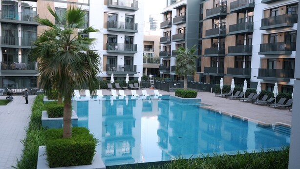 Ein modernes Hotel mit einem zentral gelegenen Schwimmbecken, umgeben von Liegestühlen und Palmen.