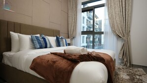 Ein Hotelzimmer mit einem großen Bett, beigefarbenen Vorhängen und Blick auf Gebäude durch ein Fenster.