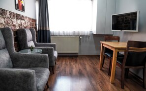 A room with a brick wall, a radiator, a grey sofa set, a wooden dining table with chairs, and a TV mounted on the wall. - Taxim No 1 Suites (Istanbul)