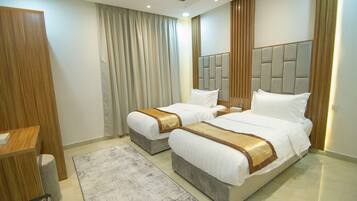 A hotel room with two beds, a wooden wardrobe, a desk, and a large window with curtains.