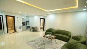 A modern living room with a green sofa, a coffee table, and a dining area with chairs. - Maqam mostaqbal for serviced apartments (Ha'il)