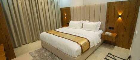 Una habitación de hotel moderna con una cama grande, cabecera de madera, mesitas de noche y un escritorio con una silla.