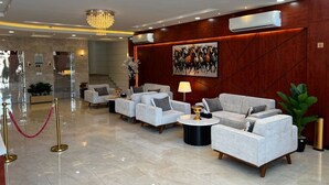 A modern lobby with a chandelier, a large painting, and a seating area with sofas and a coffee table. - Maqam mostaqbal for serviced apartments (Ha'il)