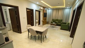 A modern living room with a green sofa, a dining area with a table and chairs, and a kitchen area with a countertop and cabinets. - Maqam mostaqbal for serviced apartments (Ha'il)
