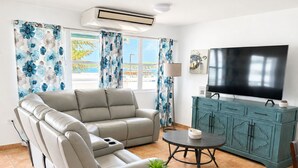 Una sala de estar con sofá, televisor, aparador y ventana con cortinas.