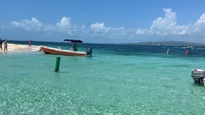 A boat docked near a beach with clear turquoise water and a distant shoreline.