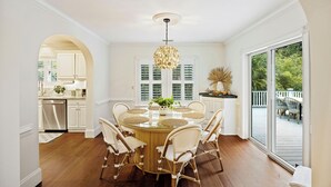 Un coin repas avec une table ronde en verre entourée de chaises en osier, un luminaire suspendu et une vue sur l’extérieur grâce à de grandes portes-fenêtres coulissantes.