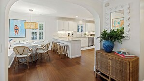 Une cuisine moderne avec des meubles blancs, un îlot central doté de tabourets de bar et un grand vase bleu posé sur une console.