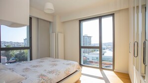 Une chambre à coucher avec un lit, de grandes fenêtres et une vue sur les immeubles.