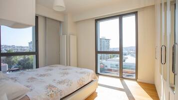 A bedroom with a bed, large windows, and a view of buildings.