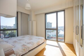 Een slaapkamer met een bed, grote ramen en uitzicht op gebouwen.