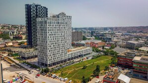 Un immeuble de grande hauteur à la façade structurée en forme de grille, entouré d’autres bâtiments et d’un parking.