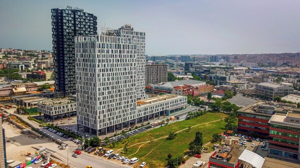 A high-rise building with a grid-like facade, surrounded by other buildings and a parking lot.