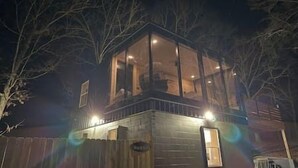A two-story building with a glass enclosure on the upper floor, surrounded by trees. - Mo-ööd House Glamping/ Floating (Licking)