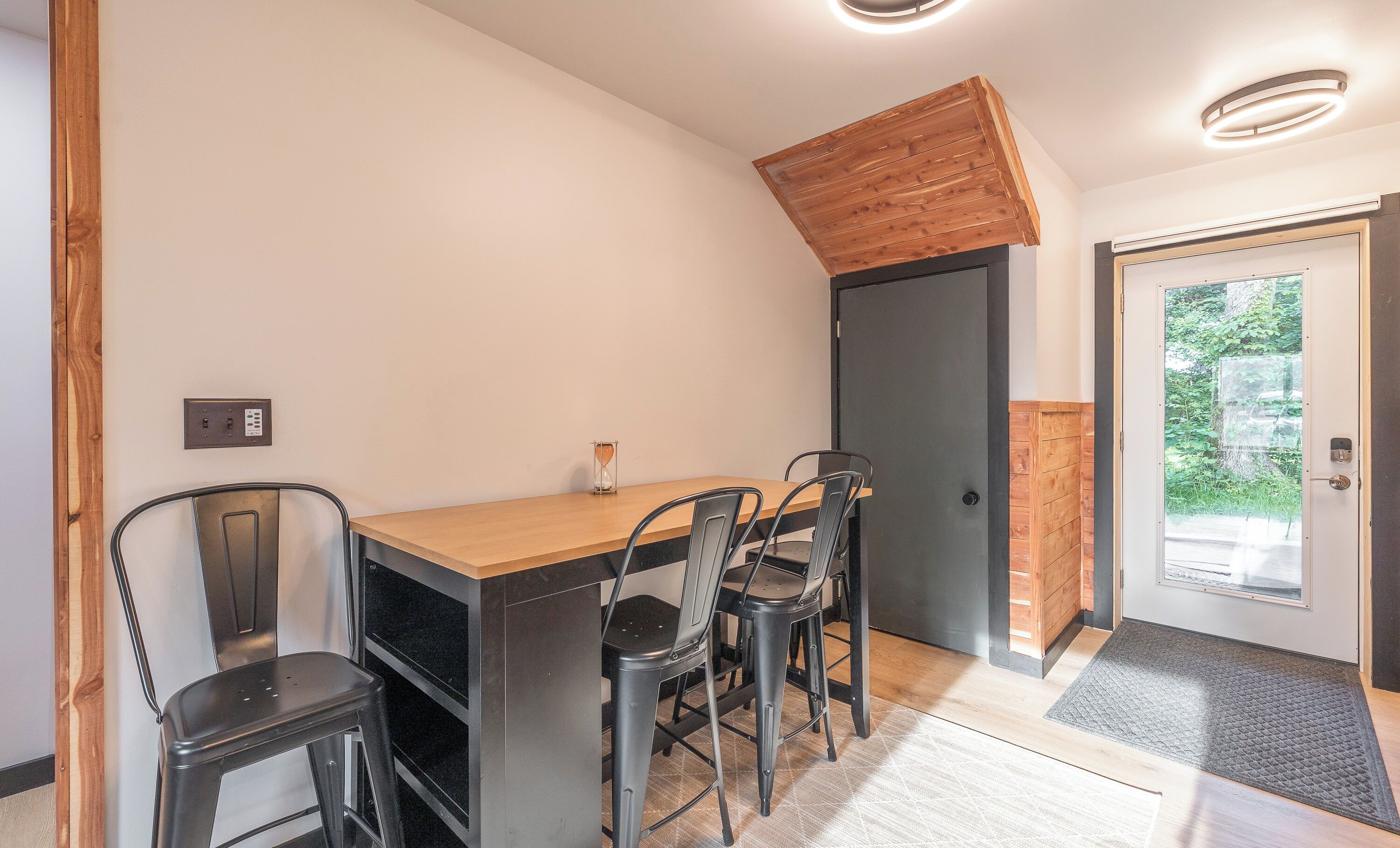 A dining area with a wooden table and four chairs, a black countertop, and a door with a glass panel.