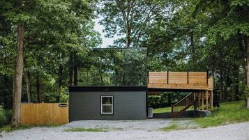 A modern cabin with a wooden deck and a small window, surrounded by trees.