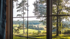 A view through a window with a grid pattern, displaying a grassy landscape with trees and a distant hill. - Floating and Glamping at Big Piney River (Licking)
