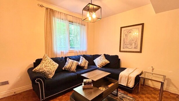 A modern living room with a dark blue sofa, patterned cushions, a wooden coffee table, and a glass side table with a vase. - Cozy One Bedroom Basement Apt with Free Parking (Markham)